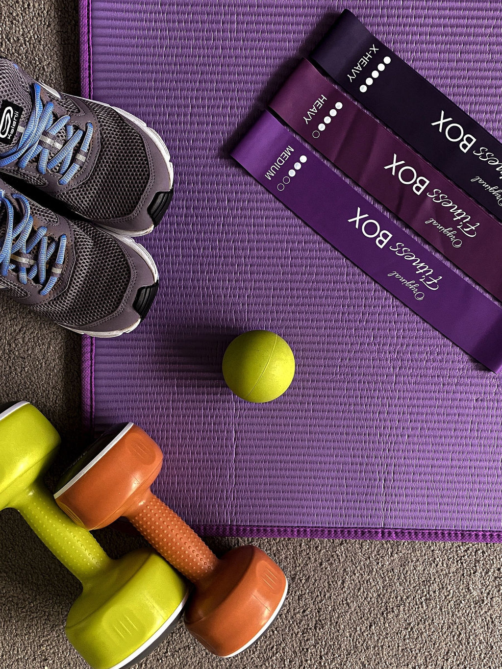 Flat lay of resistance bands, dumbbells and trainers on a fitness mat