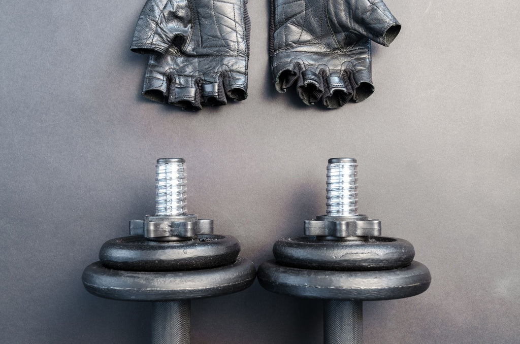 Weightlifting gym gloves with wrist support next to dumbbells on a workout mat