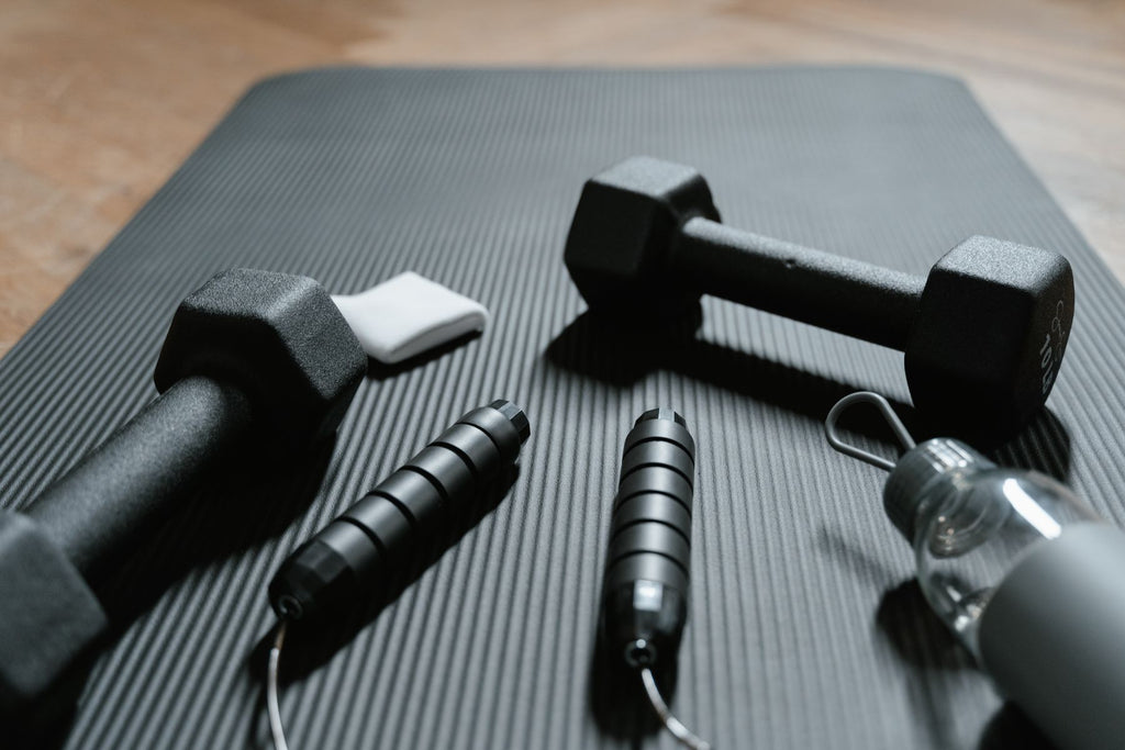 Apartment gym starter kit: dumbbells, jump rope and shaker bottle on an exercise mat